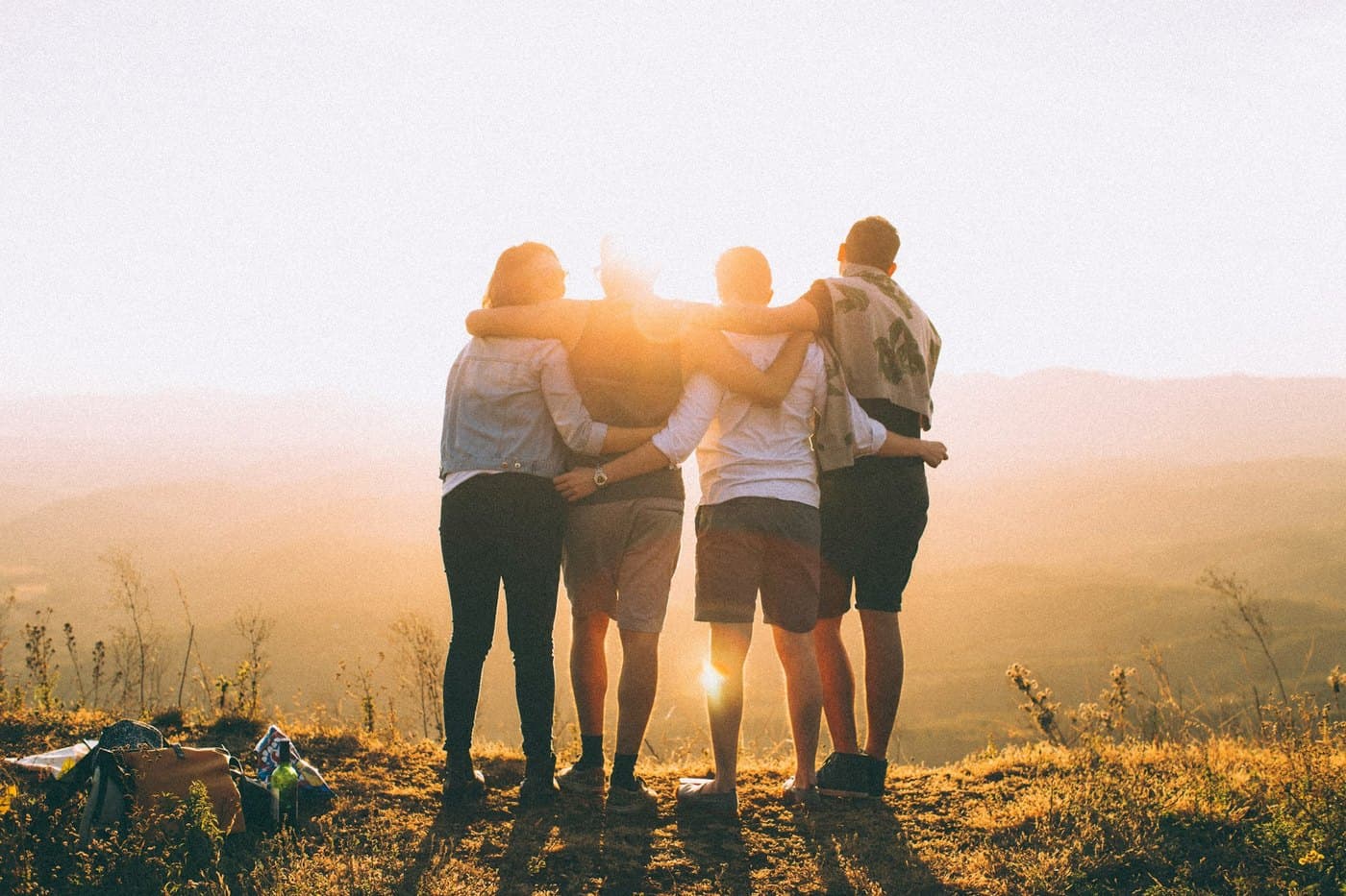 Four people arm in arm, facing the sunrise together