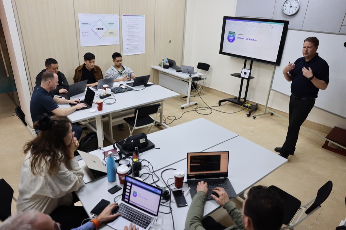 An Enterprise Movement AI-Native bootcamp in Vietnam — the room mid-build, everyone at laptops, the trainer walking the group through delivering the solution